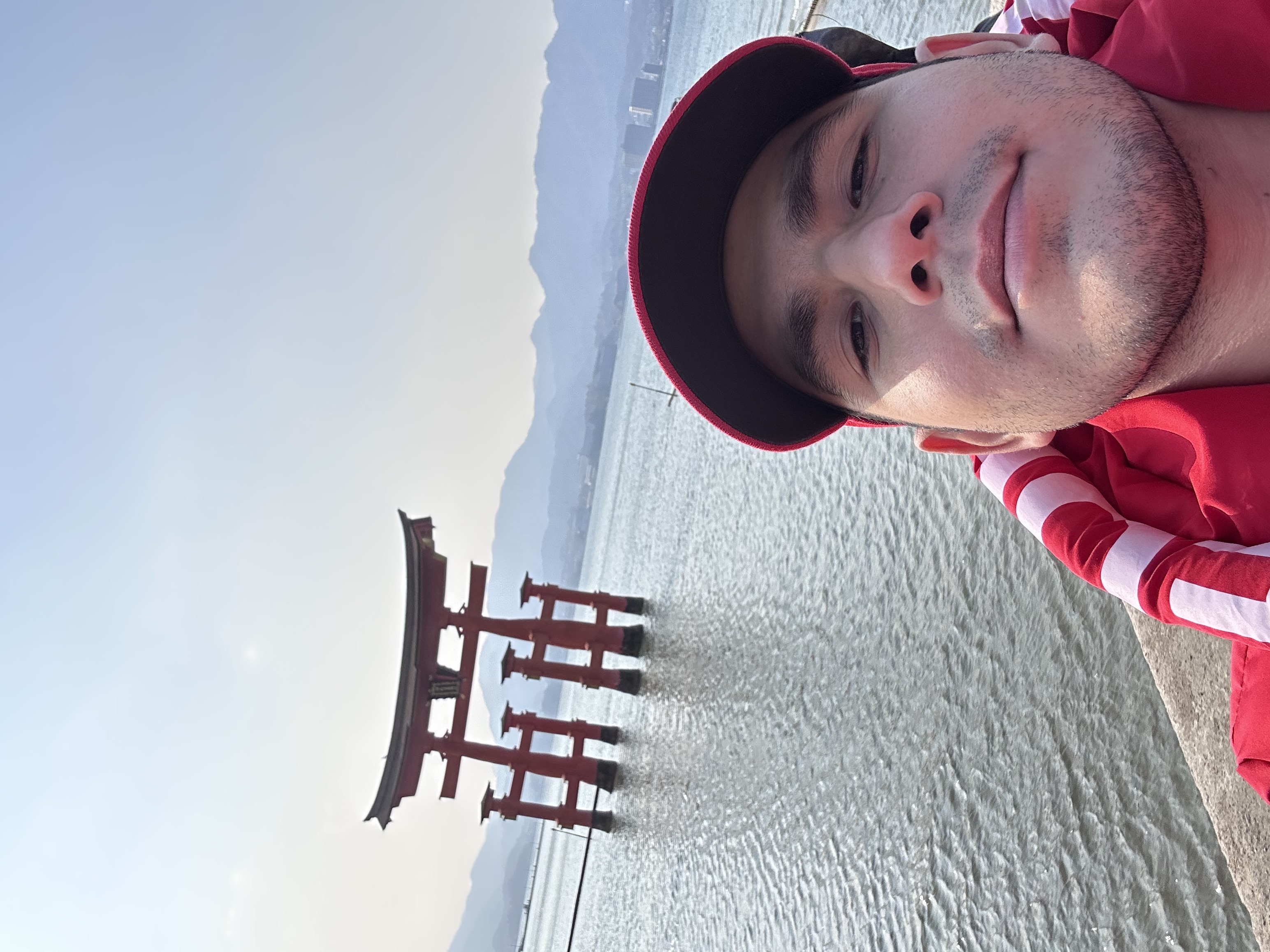 Eric by the water at Miyajima with the red torii gate behind him